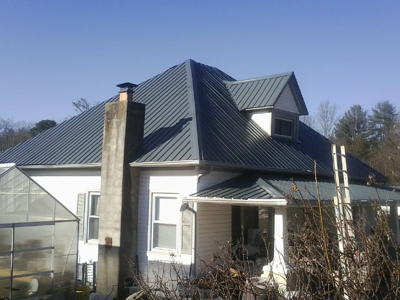 Dark blue standing seam metal roof on a white farmhouse with dormer — Slate & Tile Roof Repair by Roofing Brothers in Ruffin