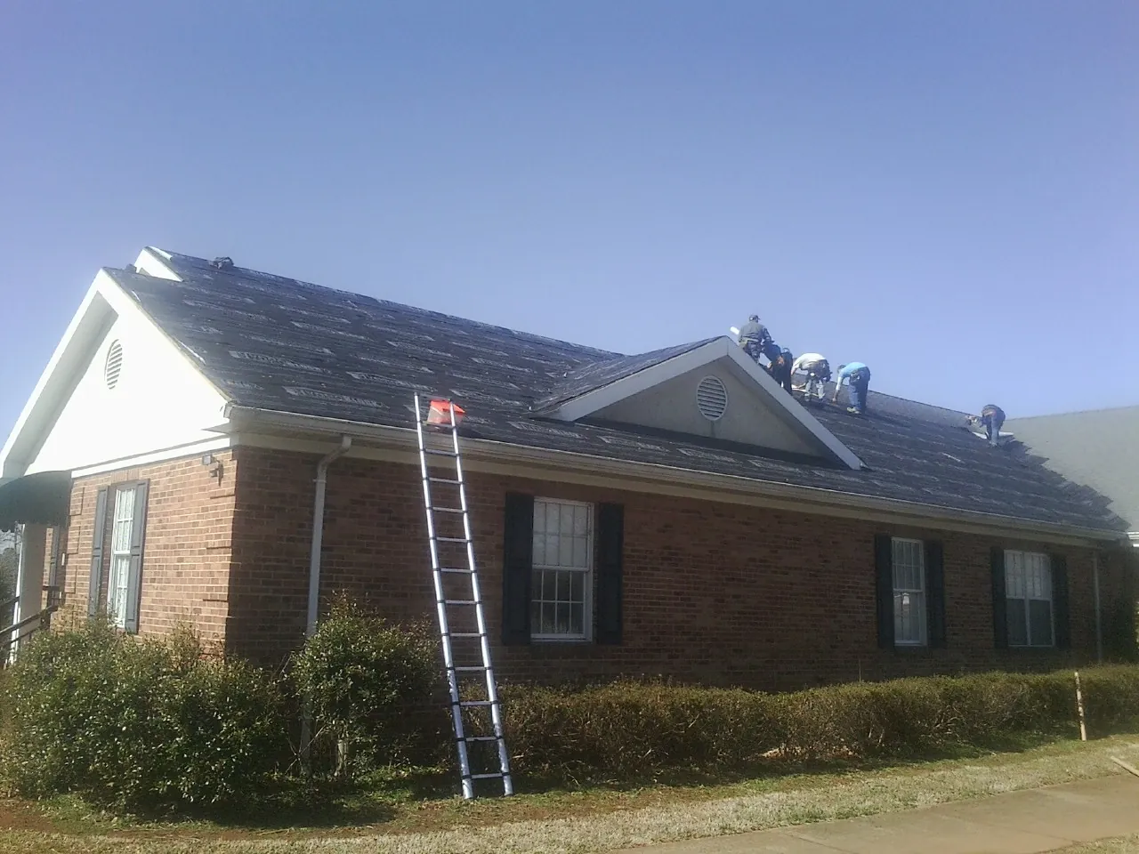 Crew tearing shingles off a brick ranch roof with a ladder set — Emergency Roof Repair work by our crew in Ruffin