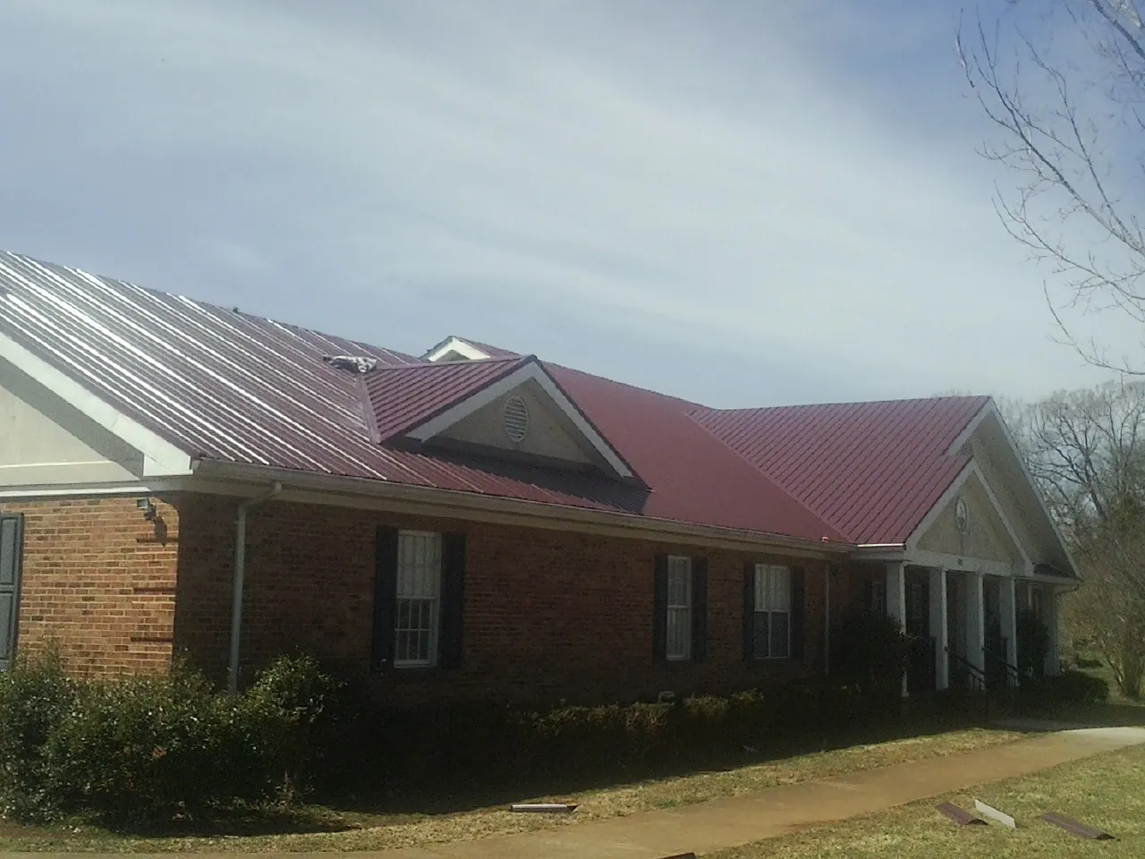 Red metal roof with gabled entries on a long brick building, from a Hail Damage Roof Repair job in Ruffin